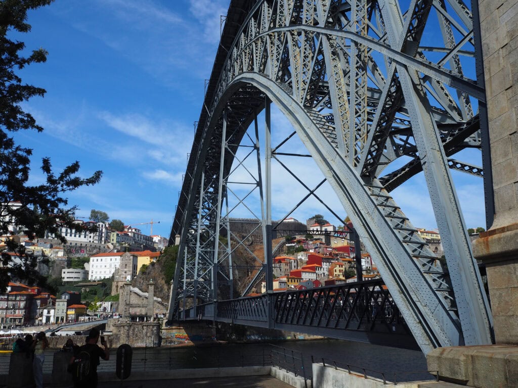 Large steel arch bridge spans a river in Porto, with colourful buildings and blue sky in the background—a perfect spot featured in any travel guide of things to do in the city.