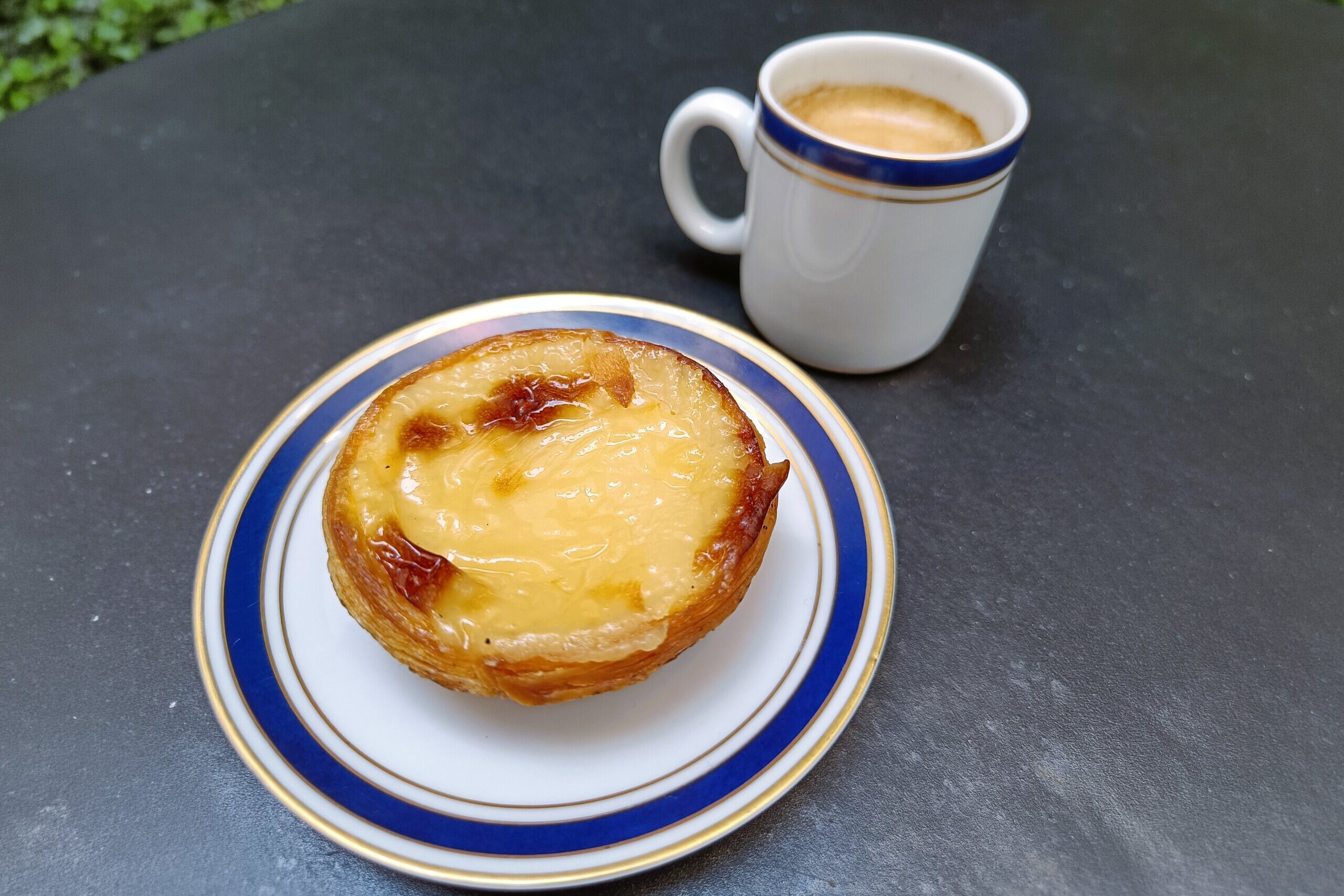 A Portuguese egg tart, said to be the best pastéis de nata in Porto, sits on a plate next to a small cup of espresso.