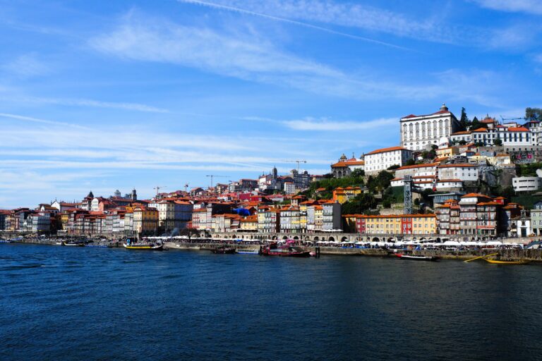 Colourful buildings line the riverside under a blue sky in Porto, a European city with historic architecture. Discover the Best Free Things to do in Porto as you stroll along these charming riverbanks.