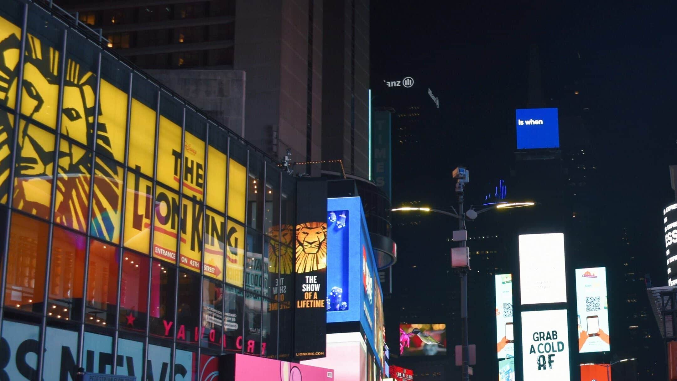 Bright billboards and colourful lights illuminate a busy Times Square street at night in New York City, capturing the vibrant energy of nearby West End musicals.