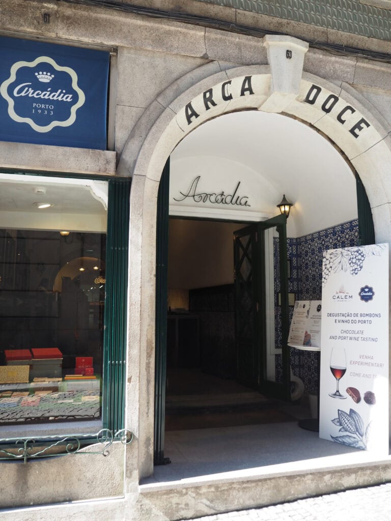 Entrance of Arcádia chocolate shop in Porto with a sign advertising port wine and chocolate tasting—a must-visit spot for anyone searching where to eat in Porto.