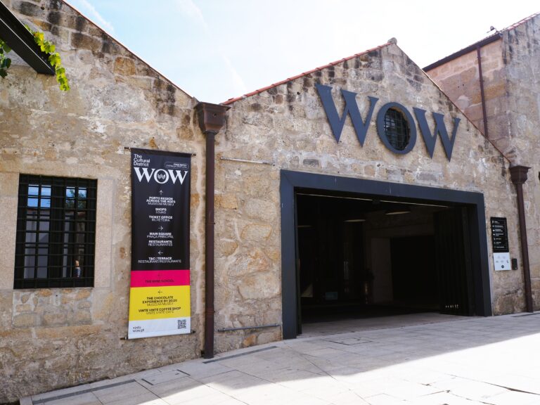 Stone building with large “WOW” letters above an open entrance, an event poster on the wall, inviting you to explore the vibrant World of Wine Porto.
