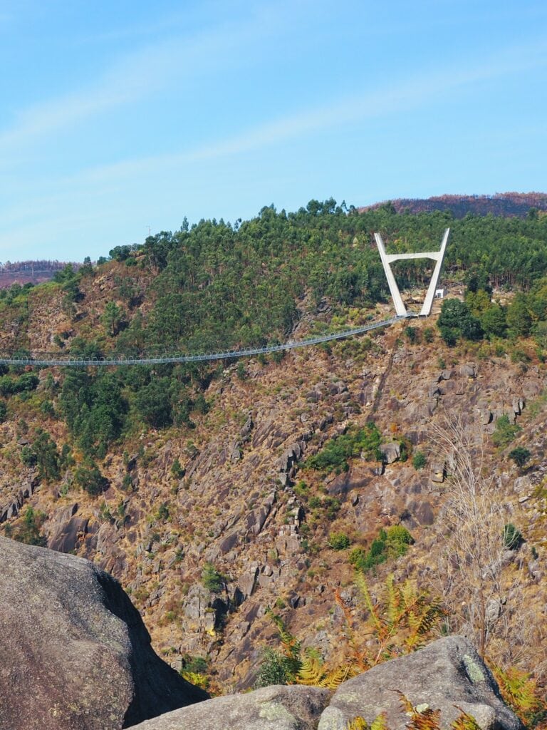 A long suspension bridge spans a rocky gorge with green forest and blue sky in the background—one of the Best Day Trips from Porto for nature lovers and adventurers alike.