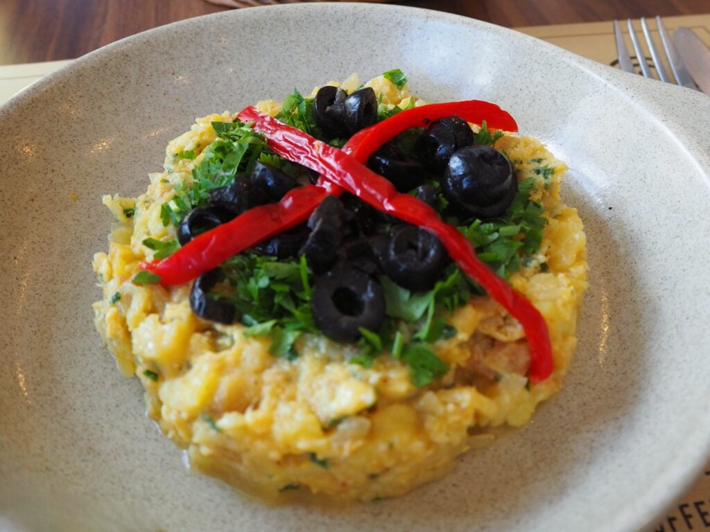 A plate of scrambled eggs topped with black olives, red pepper strips, and chopped parsley—perfect for fuelling up before exploring the Best Day Trips from Porto.
