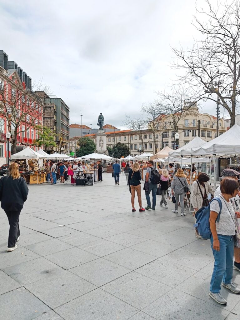 Popular markets in Porto come alive with white marquees, people shopping, and a statue in the background, even on a cloudy day.