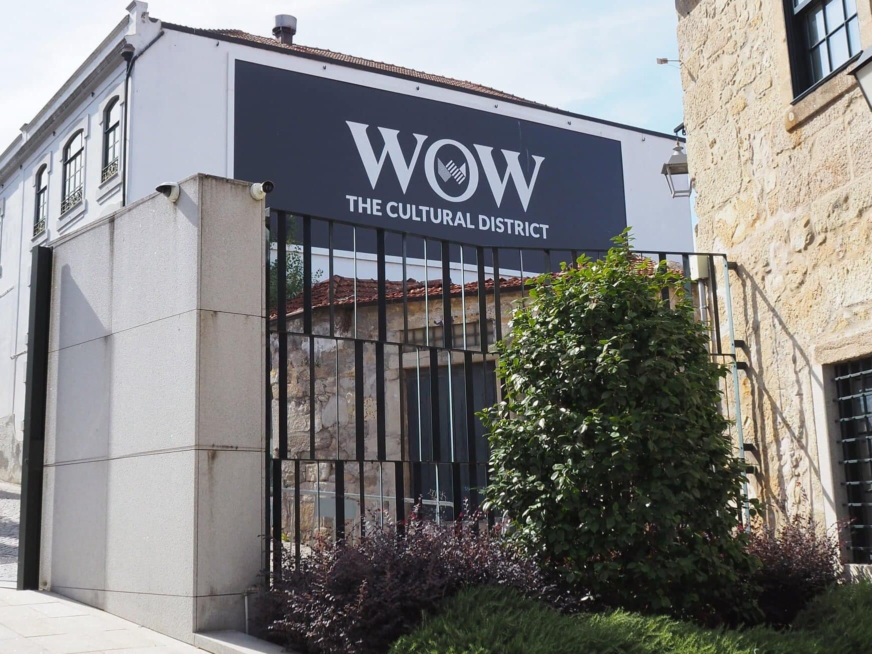 Modern building with a sign reading "WOW The Cultural District" above a gated entrance and greenery in front, located in the heart of WOW Porto, also known as the World of Wine Porto.