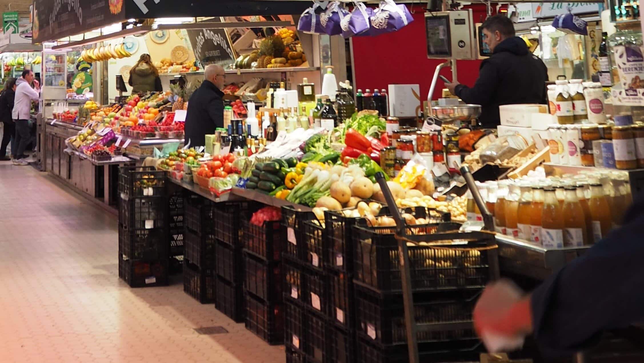 Fresh produce and bottled goods on display at an indoor market, with shoppers browsing the stalls—a highlight among the 5x Best things to Do in Avignon.
