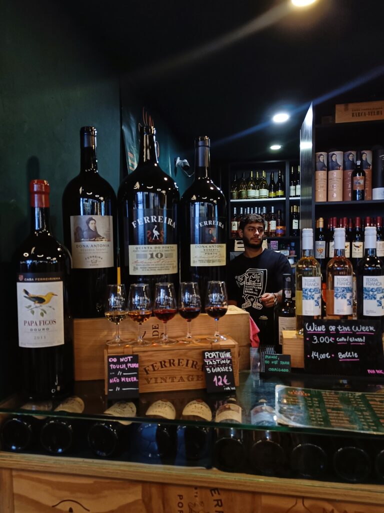 Wine bottles and glasses on a bar counter with a barman and shelves of wine in the background, capturing the vibrant atmosphere found in popular markets Porto is known for.