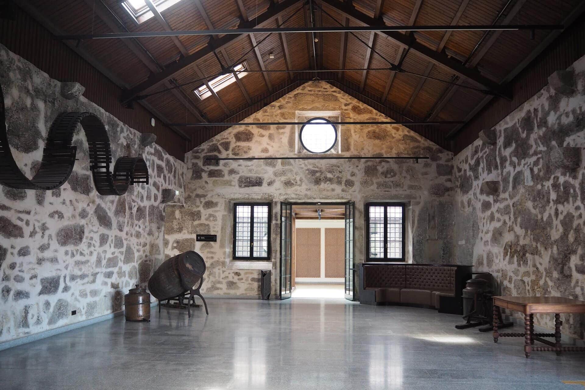 A spacious, sunlit stone-walled room with wooden ceiling beams and industrial decor elements, inspired by the vibrant style of WOW Porto (World of Wine Porto).