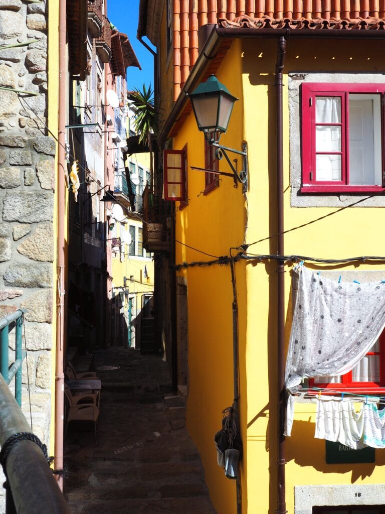 Narrow sunlit alley with yellow buildings, hanging laundry, stone walls, and a green streetlamp—perfectly capturing the charm you’d discover during one day in Porto.