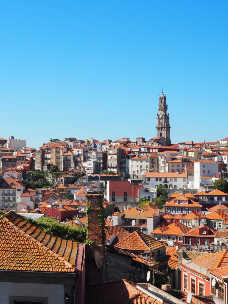 View of Porto with orange rooftops, historic buildings, and a tall church tower under a clear blue sky—a picturesque scene that perfectly captures the charm of the city. For more insights and travel inspiration, check out our tips for exploring Porto.